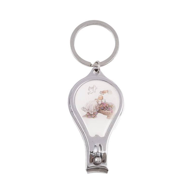 Peut inclure: Porte-cl&eacute;s argent&eacute; avec un coupe-ongles et un charme ovale blanc repr&eacute;sentant un b&eacute;b&eacute; dans une robe blanche avec une colombe et une croix au-dessus du b&eacute;b&eacute;.