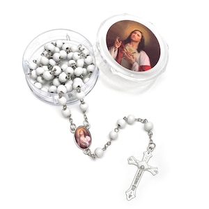 Puede incluir: Un rosario blanco con una cadena y un crucifijo plateados. Las cuentas del rosario son redondas y se guardan en un recipiente de pl&aacute;stico transparente. La tapa del recipiente presenta una imagen de Jes&uacute;s. Tambi&eacute;n hay un colgante ovalado con la imagen de una figura religiosa.