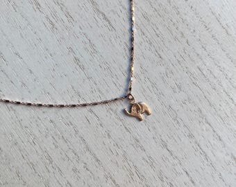 May include: A delicate rose gold necklace featuring a small elephant pendant. The chain is a fine, rectangular link design. The elephant charm is detailed with visible ears, trunk, and body. The necklace is displayed on a light-colored wooden surface.