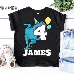 May include: Black t-shirt with a blue dinosaur wearing a party hat and holding a number 4. The dinosaur is holding balloons. The text "JAMES" is printed below the number.