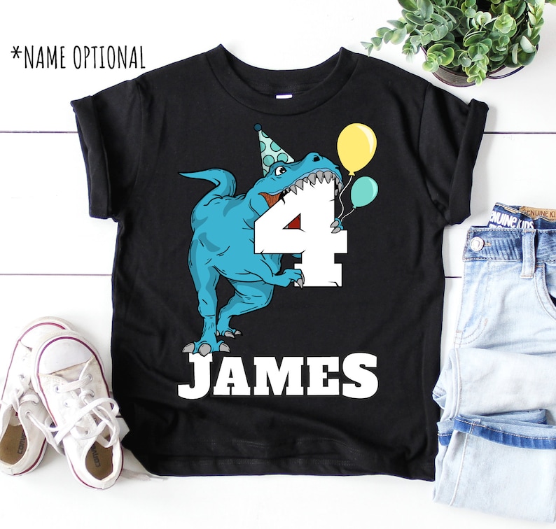 May include: Black t-shirt with a blue dinosaur wearing a party hat and holding a number 4. The dinosaur is holding balloons. The text "JAMES" is printed below the number.