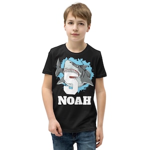 May include: Black t-shirt with a blue and white graphic of a shark with the number 5 inside its mouth. The text "NOAH" is printed below the shark.