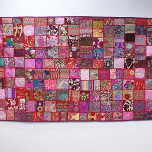 Peut inclure: Une grande courtepointe rectangulaire de patchwork avec un fond rouge et une variété de carrés colorés. Les carrés sont faits de différents tissus et ont des motifs différents, y compris des motifs floraux, géométriques et paisley. La courtepointe est décorée de perles et de paillettes.