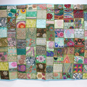 May include: A patchwork quilt featuring a range of colours and patterns, including green, blue, red, and pink. The quilt is composed of numerous small squares, each with a unique design. The quilt is bordered with a light blue trim.
