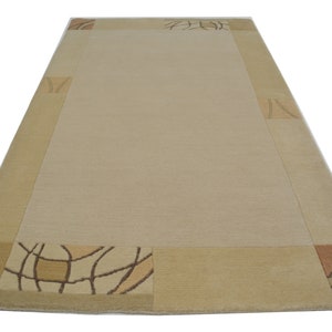 May include: A beige area rug with a light brown border and a geometric pattern in the corners. The pattern is made up of brown and beige lines.