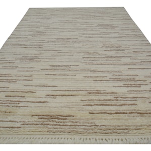May include: A cream-colored rug with a subtle brown stripe pattern. The rug has a fringe border.