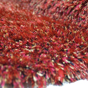 Op de afbeelding: Close-up van een rood, goud en zwart shagtapijt met een zachte, pluche textuur.