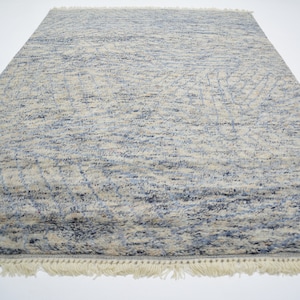 May include: A blue and cream patterned rug with a fringe border. The rug has a subtle abstract design.