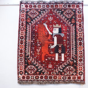 May include: A red, black, and white rug with a traditional Persian design. The rug features a central image of a person in a crown standing next to a lion.