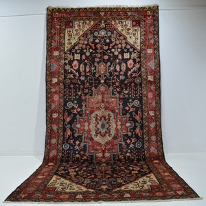 May include: An intricately patterned rug with a central medallion design. The rug features a dark navy blue field with red, beige, and blue accents. The border is a contrasting red with detailed floral motifs. The rug is displayed against a white background.