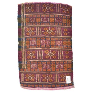 May include: A vintage rug with a geometric pattern in shades of red, orange, blue, and green. The rug has a fringe border.