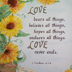 May include: Watercolor painting of sunflowers with a quote about love from 1 Corinthians 13:7-8. The quote reads "LOVE bears all things, believes all things, hopes all things, endures all things. LOVE never ends." The painting is signed "Cindy & George 5-24-14" and "M. Scharyj-Douglas".