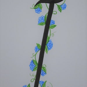 May include: A black calligraphic letter I with a vine of blue flowers and green leaves winding around it.