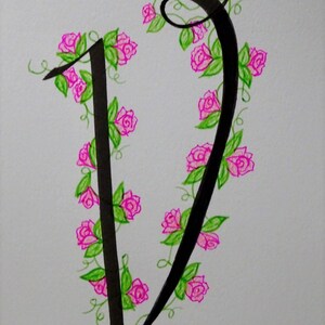 May include: A black calligraphic letter V with a vine of pink roses and green leaves wrapping around it.