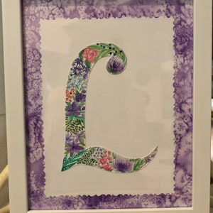 May include: A framed watercolor painting of the letter L, decorated with purple, pink, and green flowers. The frame has a purple scalloped border.
