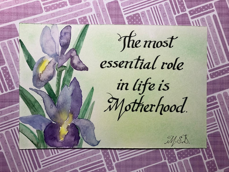 May include: A watercolor painting of purple irises with green leaves on a light green background. The text "The most essential role in life is Motherhood." is written in black cursive script. The painting is signed "M.S."
