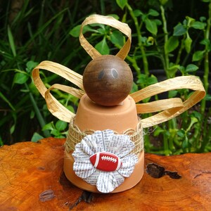 Peut inclure: Un pot de fleurs en terre cuite avec une boule en bois brun sur le dessus, d&eacute;cor&eacute; d'un ruban en toile de jute brun et d'une fleur en papier avec un ballon de football rouge et blanc au centre. Le pot est entour&eacute; d'un ruban dor&eacute;.