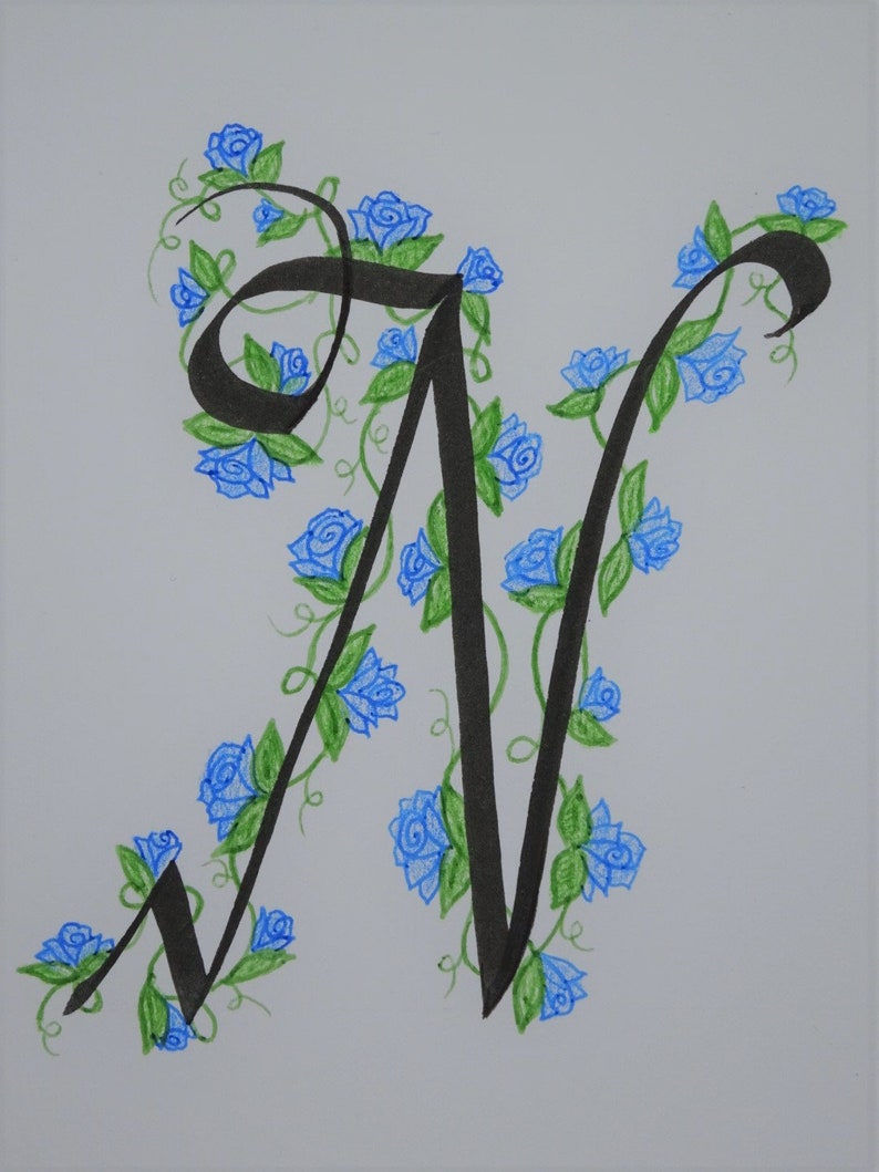 May include: A black calligraphic letter N with blue and green floral embellishments. The letter is surrounded by blue roses and green leaves.