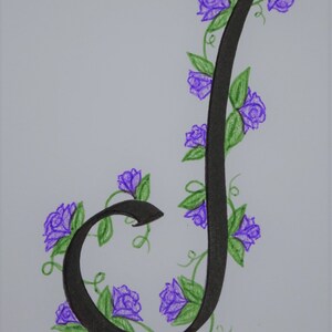 May include: A black calligraphic letter J with a vine of purple flowers and green leaves winding around it.