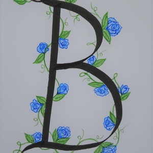 May include: A black calligraphic letter B with a vine of blue roses and green leaves winding around it.