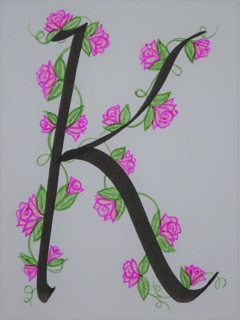 May include: A black calligraphic letter K with a vine of pink roses winding around it. The roses have green leaves and stems.