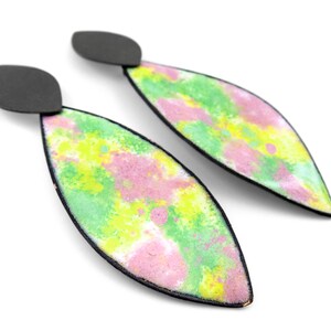 May include: A pair of dangle earrings with a black metal base and a green, pink, and yellow abstract design.