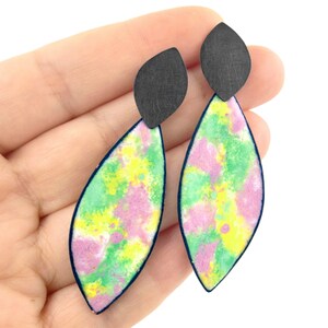 May include: A pair of dangle earrings with a green, pink, and yellow watercolor design. The earrings have a black teardrop-shaped top.