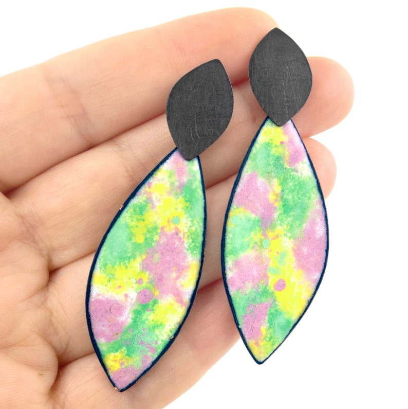 May include: A pair of dangle earrings with a green, pink, and yellow watercolor design. The earrings have a black teardrop-shaped top.