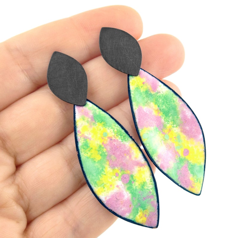 May include: A pair of dangle earrings with a black top and a colorful, abstract design. The earrings are painted with shades of pink, green, and yellow.