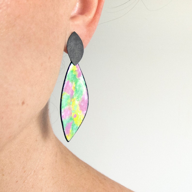 May include: A pair of dangle earrings with a black top and a colorful bottom. The bottom of the earrings are a teardrop shape with a pink, green, and yellow tie-dye pattern.