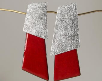 Peut inclure: Une paire de boucles d'oreilles pendantes au design trapézoïdal. Chaque boucle se compose d'une partie supérieure à la finition argentée brossée et d'une partie inférieure à la finition émaillée rouge vif, lisse et brillante.