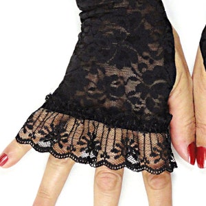 Puede incluir: Guantes sin dedos de encaje negro con un borde de volantes. Los guantes son transparentes y tienen un patr&oacute;n floral.