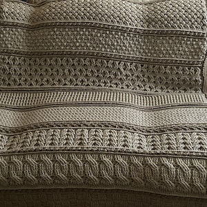 May include: A brown crocheted throw blanket with a variety of stitch patterns. The blanket is made with a thick yarn and has a soft, textured feel.