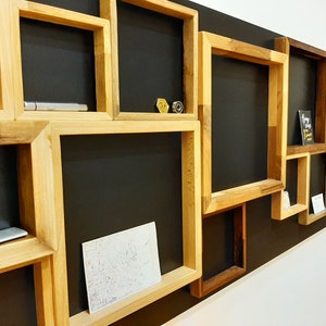 Peut inclure: Une exposition murale avec plusieurs cadres en bois de différentes tailles et formes. Les cadres sont disposés en chevauchement et sont montés sur un fond noir. Certains cadres contiennent de petits objets, comme un stylo, un petit objet métallique et un morceau de papier.