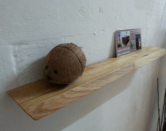 Puede incluir: Una estantería de madera con un acabado natural, montada en una pared blanca. Un coco marrón se encuentra sobre la estantería, y una tarjeta de visita con el texto "Free-Design" está colocada sobre la estantería.