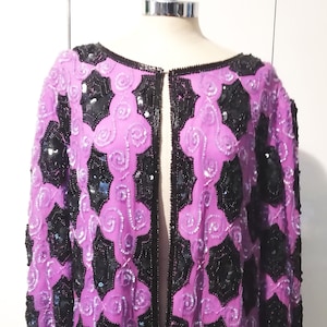 May include: A purple and black sequined jacket with a long, open front. The jacket is decorated with a geometric pattern of black sequins on a purple background.