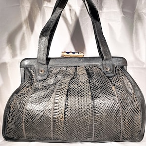 Op de afbeelding: Een zwarte leren handtas met een slangenhuidpatroon en een gouden sluiting. De tas heeft twee bovenste handvatten.