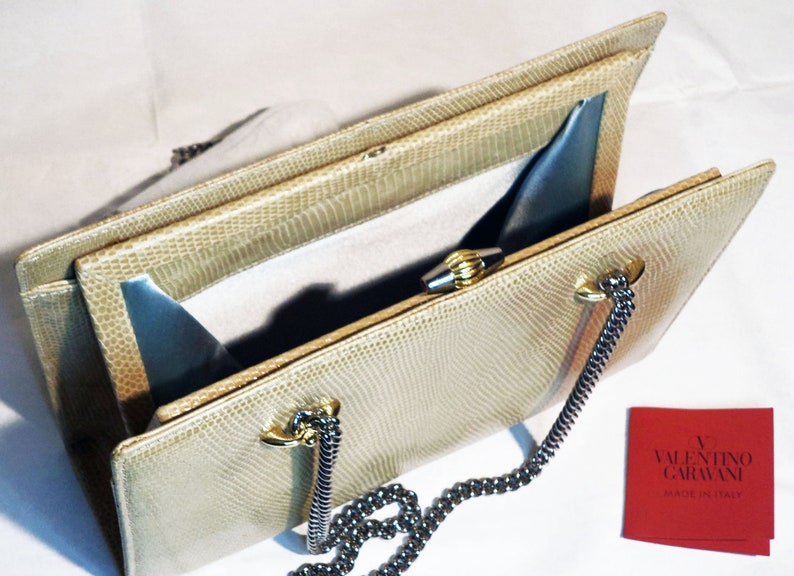 Puede incluir: Un bolso de mano de piel de serpiente beige con cierre de broche dorado y correa de cadena. El bolso est&aacute; abierto y el interior est&aacute; forrado con un tejido azul claro. El bolso tiene una etiqueta que dice "Valentino Garavani Made in Italy".