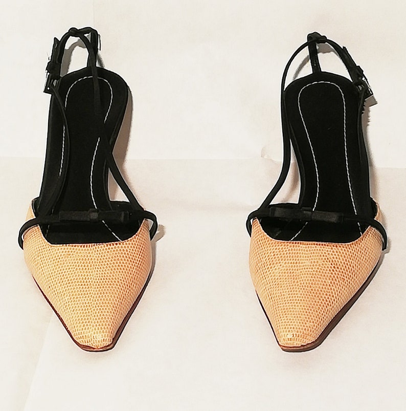 Puede incluir: Un par de zapatos de tac&oacute;n alto para mujer. Los zapatos tienen una punta afilada y un exterior texturizado de color beige claro. El tac&oacute;n y las correas son negros, con un peque&ntilde;o lazo en la correa delantera. Los tacones miden aproximadamente 7,6 cm de alto.
