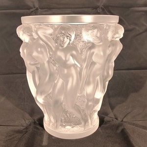 May include: A frosted glass vase with a design of five figures in relief. The figures are nude and appear to be dancing or celebrating.