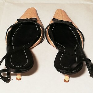 Puede incluir: Un par de zapatos de tac&oacute;n beige con tiras traseras, puntera afilada y peque&ntilde;os lazos negros. Los zapatos tienen plantillas negras y correas en los tobillos. Los tacones son de color marr&oacute;n claro.