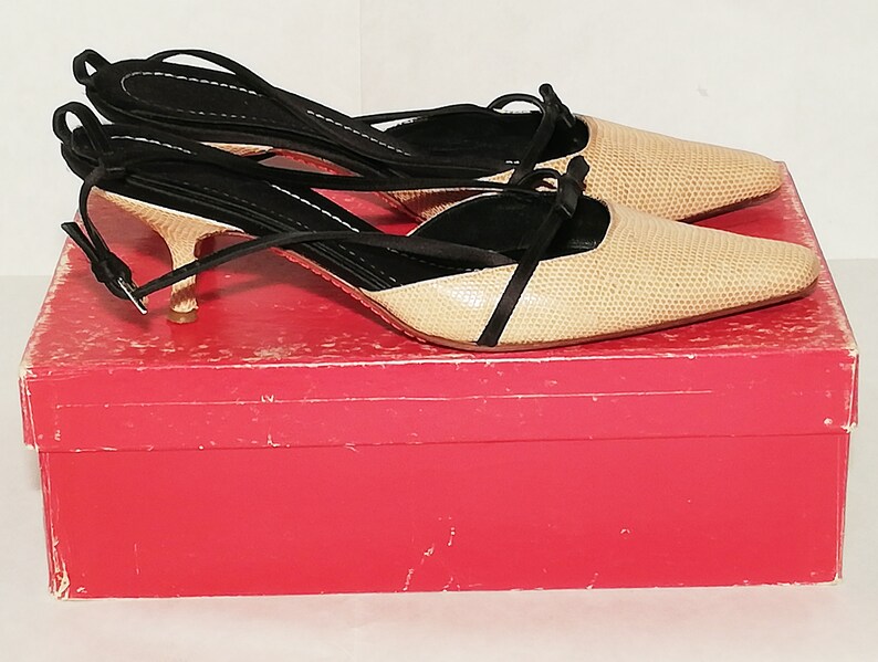 Puede incluir: Un par de zapatos de tac&oacute;n slingback beige y negro con estampado de reptil, sobre una caja roja. Los tacones tienen punta afilada, tiras finas y un tac&oacute;n peque&ntilde;o. Las correas negras se envuelven alrededor del tobillo.