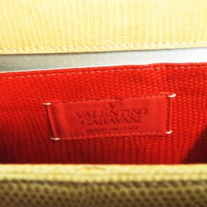 Puede incluir: Primer plano del interior de un bolso de mano de cuero rojo con una etiqueta de Valentino Garavani. La etiqueta es blanca con texto negro y un peque&ntilde;o logotipo de coraz&oacute;n rojo.