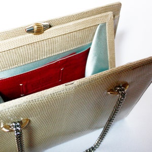 Puede incluir: Un bolso de mano beige de piel de serpiente con cierre dorado y cadena. El interior est&aacute; forrado con tela azul claro y tiene un bolsillo rojo.