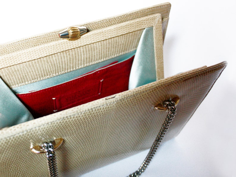 Puede incluir: Un bolso de mano beige de piel de serpiente con cierre dorado y cadena. El interior est&aacute; forrado con tela azul claro y tiene un bolsillo rojo.