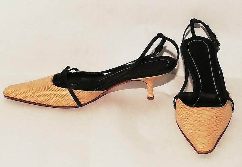 Puede incluir: Un par de zapatos de tac&oacute;n slingback beige y negro. Los zapatos de punta tienen una pala beige texturizada y una correa negra que se envuelve alrededor del tobillo. Los tacones miden aproximadamente 5 cm de alto.