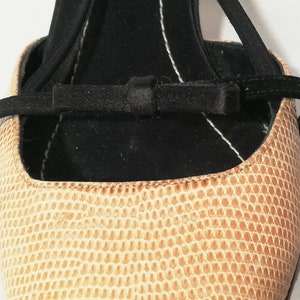 Puede incluir: Primer plano de un zapato beige texturizado con una correa negra y un detalle de lazo. El zapato tiene un patr&oacute;n similar al de un reptil y un interior negro. La correa se envuelve alrededor del tobillo.