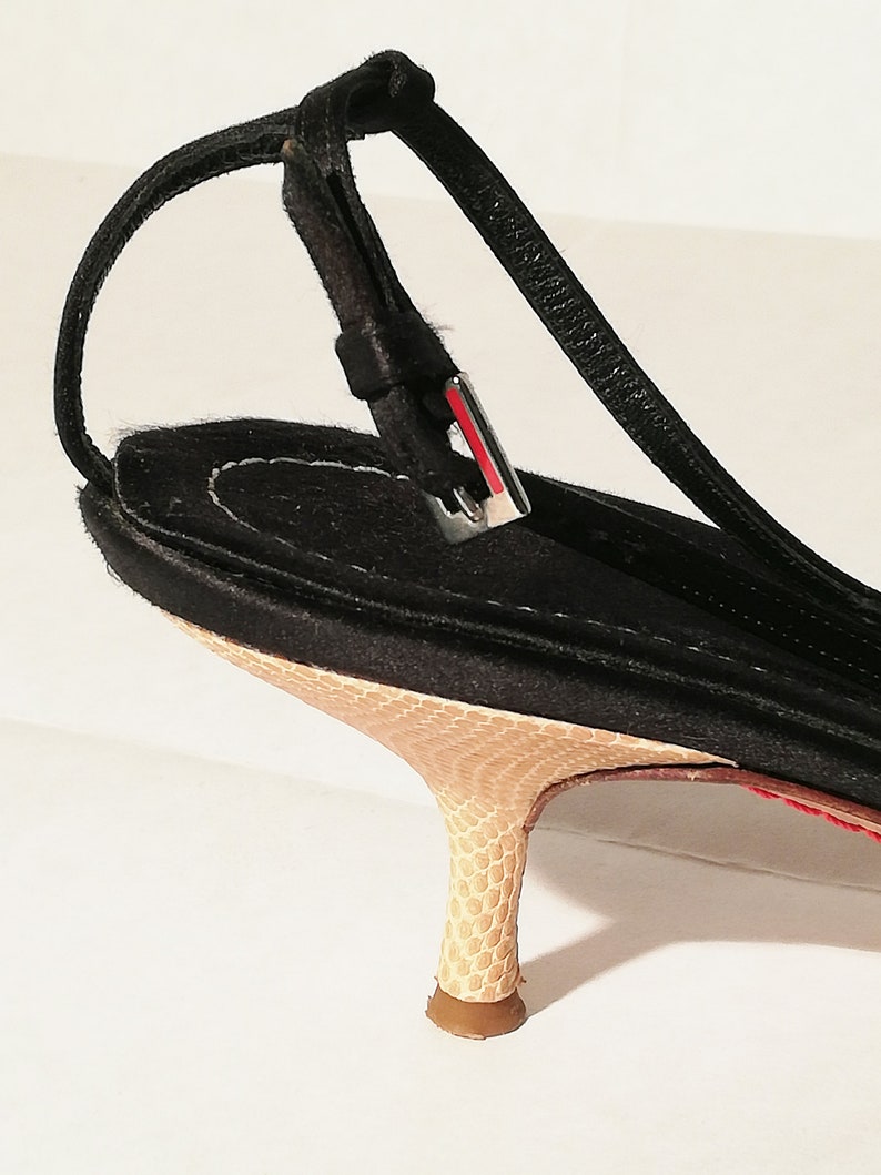 Puede incluir: Sandalia negra con tira trasera, tac&oacute;n y suela con estampado de piel de serpiente. El tac&oacute;n mide aproximadamente 6,35 cm de alto. La sandalia tiene una fina correa y una hebilla plateada con detalles rojos.