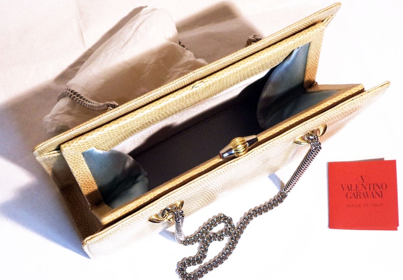 Puede incluir: Un bolso de mano de piel de serpiente beige con una correa de cadena plateada y un cierre dorado. El bolso est&aacute; abierto y el interior est&aacute; forrado con un tejido azul claro. El bolso tiene una etiqueta que dice "V Valentino Garavani Made in Italy."
