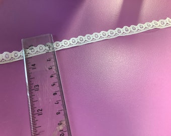 May include: White lace trim with a scalloped edge and a repeating circle pattern. The trim is measured against a ruler, showing it is approximately 1 inch wide.